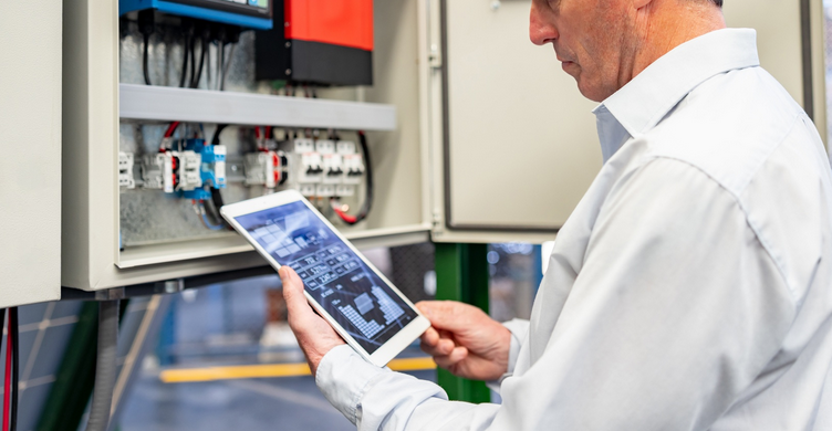 Ein Mann mit einem Tablet in der Hand vor einem Schaltschrank. Symbolbild.