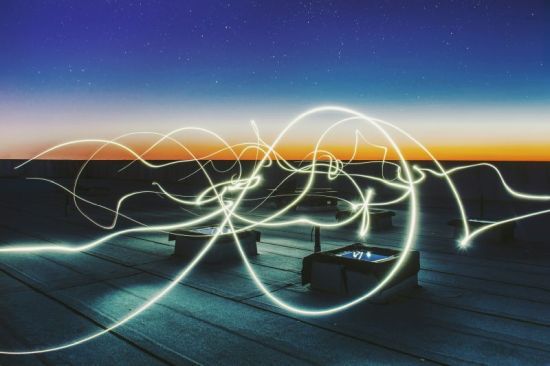 Verschiedene gelbliche Lichstrahlen fliegen durchs Bild. Es ist Einbruch der Nacht mit einem hellen Streif am Horizont.